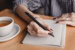 © Olena - Woman hand writing note pad on wood table in coffee shop