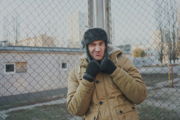 Happy handsome young man in cap with earflaps. The young man in the fur hat. a young guy standing on the street on a cloudy day. emotional portrait of a student. street style