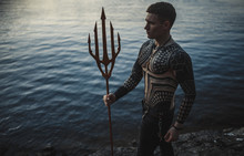 A Young Man With A Trident Against The Background Of Water.