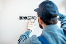 Electrician In Uniform Mounting Electric Sockets On The White Wall Indoors