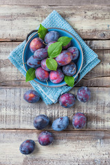 Wall Mural - Plums overhead fresh colorful arrangement on blue plate and kitchen cloth on wooden table in studio