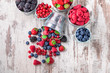 Berries fresh colorful arrangement in tin cans and some spilled fruit on old rustic white wooden table in studio