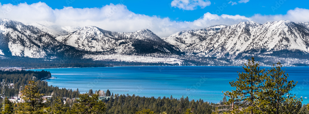 Panoramic view towards Lake Tahoe on a sunny clear day; the snow covered Sierra mountains in the background; evergreen forests in the foreground - obrazy, fototapety, plakaty 