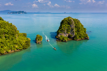 Aerial drone view of longtail boats passing between 2 small, rocky tropical islands