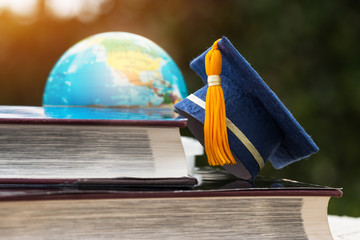 Graduate or Education knowledge learning study abroad concept : Blue Graduation cap on opening textbook with blur of america earth world globe model map in Library room of campus, Back to School
