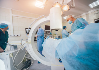 Wall Mural - Process of trauma surgery operation. Group of surgeons in operating room with surgery x-ray equipment.