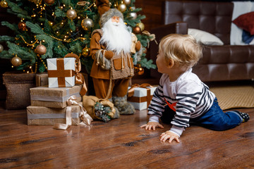 Small child looks at the doll Santa Claus on the background of Christmas tree