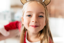 Cute Young Girl Wearing Costume Reindeer Antlers, Smiling And Looking At Camera. Happy Kid At Christmas Time.