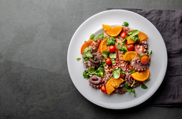 Whole octopus salad with orange, tomatoes and cress salad on white plate. Top view