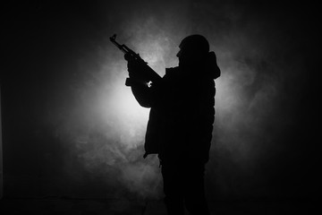 silhouette of man with assault rifle ready to attack on dark toned foggy background or dangerous ban