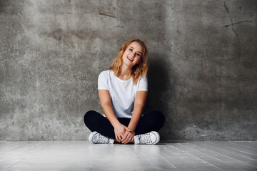 Wall Mural - girl 20s wearing white t-shirt and sneakers sitting with legs crossed on the floor