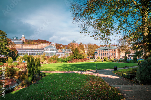 Fotomural Lovely view of Buxton Park in Autumn, showing the calm pond and beautiful autumnal trees as well as the stone architecture of the town
