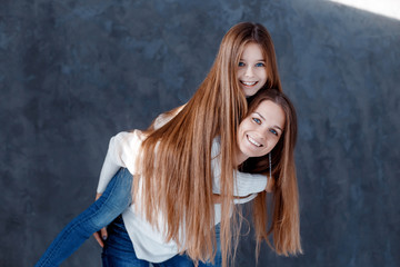 Stylish beautiful mother and a cute daughter with blue eyes in studio hugging and having fun. family, love concept