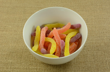 Wall Mural - Yellow, orange and purple sour gummy worms candy in white bowl on burlap