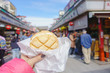 © picment - Asakusa,Tokyo - October 31 2018 : Woman hand holding melon pan at Nakamise Shopping Street Asakusa temple. Landmark in Japan. Japanese Language.