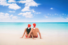 Christmas Beach Vacation Holidays Santa Hat Couple Relaxing From Behind Sitting On White Sand Blue Sky Background For Text Advert For Holiday Season.