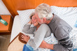 © simona - retired aged couple 70 years old in the bed at early morning kissing and waking up together with love and romance - people live forever together concept for caucasian man and woman