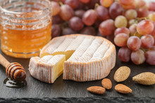 Delicatessen Soft Fragrant Cheese With Mold, Honey, Almonds And Red Grapes On A Black Slate Plate. Snacks For Gourmets