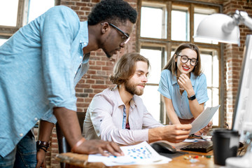 Wall Mural - Group of young multi ethnicity coworkers dressed casually working together with computers and documents at the modern office interior