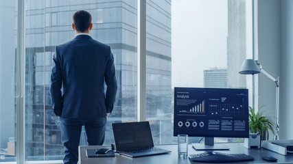 Confident Businessman in a Suit Contemplating Business Deal in His Office, Looking out of the Window. Window Has Panoramic View on Big City Business District.