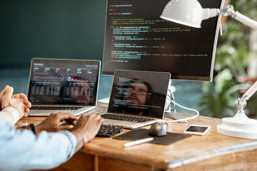 programmers writing a program code sitting at the workplace with three monitors in the office. cropp
