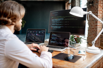 Wall Mural - young male programmer writing a program code sitting at the workplace with three monitors in the off