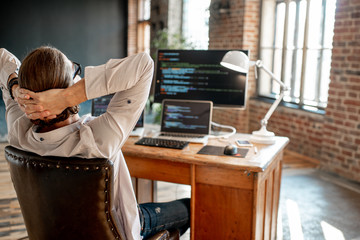 Wall Mural - young male programmer relaxing during the work with program code sitting at the workplace with three