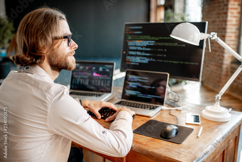 Cuadros en Lienzo Young male programmer writing a program code sitting at the workplace with three