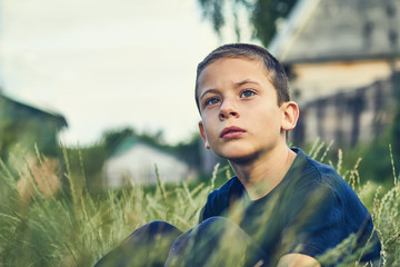the child is sitting in the grass outdoors and looking serious look into the distance.