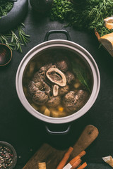 Wall Mural - Broth of beef meat shin with bone in cooking pot on dark kitchen table background with ingredients for soup, top view. Meat broth or stock. Clean low-calorie food and eating concept