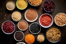Various superfoods in smal bowls on dark rusty background. Superfood as rice, lentil, beans, peas, goji, flaxseed, buckwheat, couscous, chickpeas Top view Flat lay