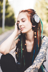 young girl with tattoo and dreadlocks listening to music in the park