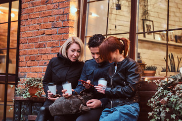 Wall Mural - Three happy friends having a break with coffee sitting near a cafe outside.