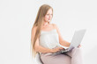 © xartproduction - Portrait of a young blonde girl sitting on a chair against a white wall and working at a laptop