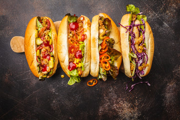 Hot dogs with assorted toppings on a dark background, top view, copy space.