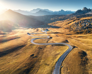 Wall Mural - Winding road in mountain valley at sunset in autumn. Aerial view of asphalt road in Passo Giau. Dolomites, Italy. Top view of roadway, mountains, meadows with orange grass, blue sky and gold sunlight