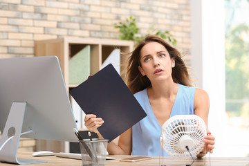 Businesswoman suffering from heat in front of small fan at workplace