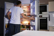 Young man looking for food in refrigerator at night