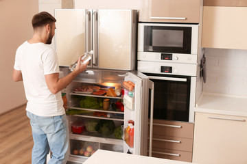 Sticker - Young man taking bottle of water from refrigerator in kitchen