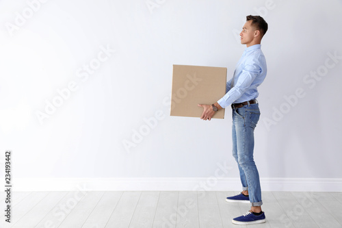 Fotografía Full length portrait of young man carrying heavy cardboard box near white wall