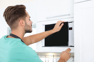 Wall Mural - Young man using modern microwave oven at home