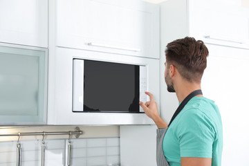 Young man using modern microwave oven at home