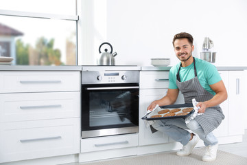 Sticker - Young man holding baking sheet with cookies near oven in kitchen