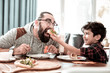 © zinkevych - High five. Emotional modern father giving high five his funny little son while eating pizza together