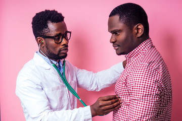 happy male african medical surgeon cardiologist doctor in a white coat and patient on a pink background in the studio.