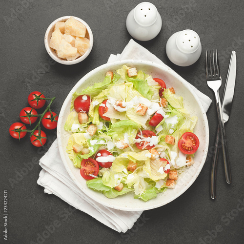 Fotografía Caesar salad on white plate over black concrete background