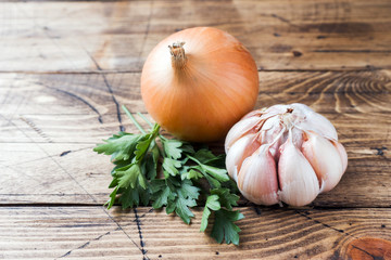 Head of garlic, onion and parsley on wooden background.