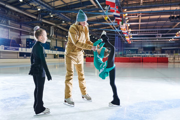 Portrait of two girls learning to figure skate during training with female coach in indoor rink