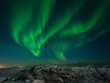 Beautiful stripes of the northern lights, aurora in the night sky above the snow covered hills.