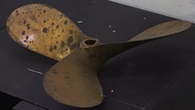 A High Angle, Medium Shot Of A Three Bladed, Rusty, Boat Engine Propeller.